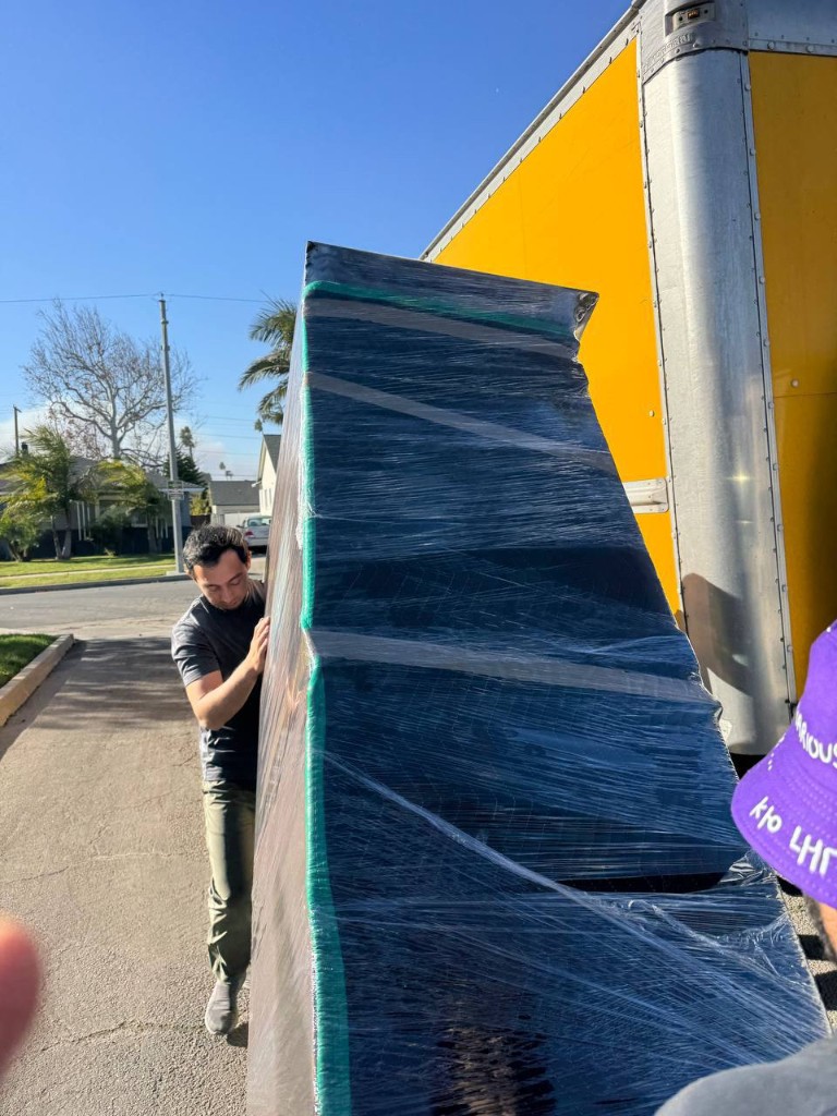 Mover carefully guiding a wrapped high-value item beside a truck
